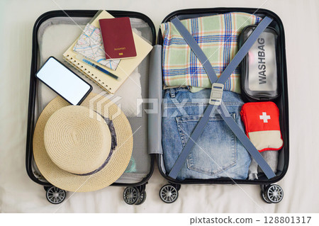 top view of open suitcase on bed for packing, preparing for summer holidays abroad trip with passport, map, hat, travel medicine first aid kit, clothing, phone mockup with copy space for advertise top view of open suitcase on bed for packing, preparing for summer holidays abroad trip with passport, map, hat, travel medicine first aid kit, clothing, phone mockup with copy space for advertise 128801317
