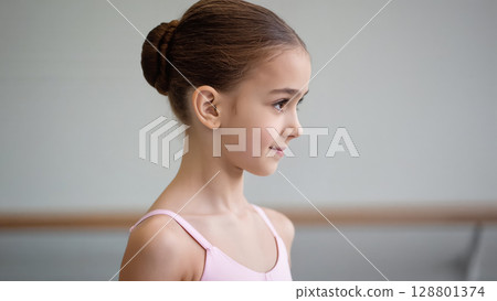 Portrait of a young ballerina in a pink leotard with a neat bun, standing in a dance studio. Graceful and focused expression. Portrait of a young ballerina in a pink leotard with a neat bun, standing in a dance studio. Graceful and focused expression. 128801374