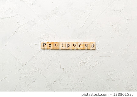Postponed word written on wood block. Postponed text on cement table for your desing, concept Postponed word written on wood block. Postponed text on cement table for your desing, concept 128801553
