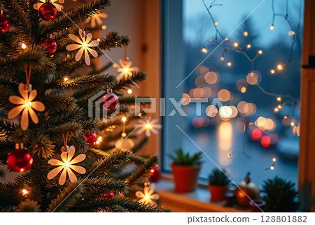 Cozy home atmosphere for the Christmas holidays. A festive Christmas tree with red balls and garlands is beautifully reflected in the window glass. 128801882