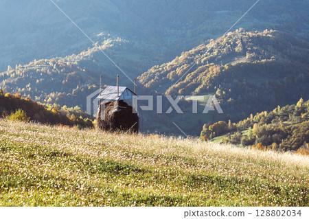 Morning landscape with haystack and glowing forest in autumn mountains 128802034
