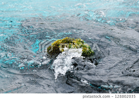 Moss-covered rock in pure Icelandic stream with swirling water. Concept of sustainability, minimalism, environmental balance, clean energy and fragile natural beauty. 128802035