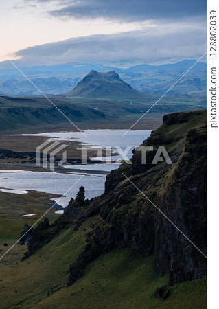 Scenic volcanic cliffs and river delta in South Iceland under dramatic skies. Concept of natural energy, exploration, raw beauty, geological power and Nordic adventure. 128802039