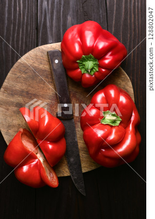 Slicing fresh red sweet bell peppers on rustic wooden cutting board 128802047