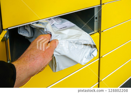 Hand Collecting Parcel from Yellow Locker at Self-Service Pickup Station Outdoors 128802208