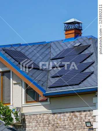 Modern House with Solar Panels on Blue Roof and Brick Facade Under Clear Blue Sky on a Sunny Day 128802211