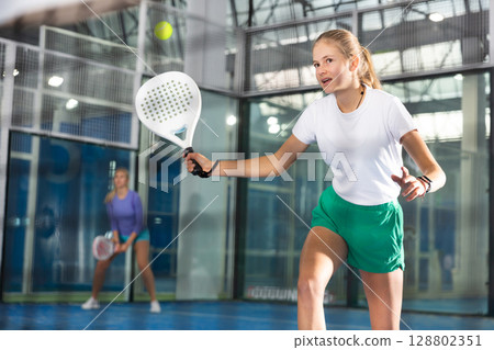Expressive resolved fit teenage girl playing paddle ball friendly match on small closed court. Concept of competition emotions. 128802351