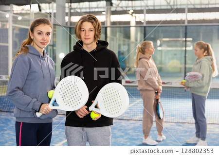 Portrait of a young woman with a boy-athlete standing with padel rackets and balls 128802353