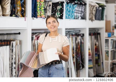 Girl scrutinizes examine collection of samples of sheathing fabric in furniture store Girl scrutinizes examine collection of samples of sheathing fabric in furniture store 128802406