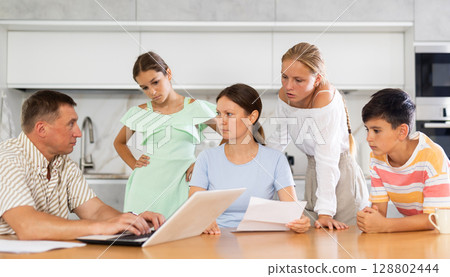 Man with laptop does remote work, frustrated wife reads letter, and alarmed children stand nearby Man with laptop does remote work, frustrated wife reads letter, and alarmed children stand nearby 128802444