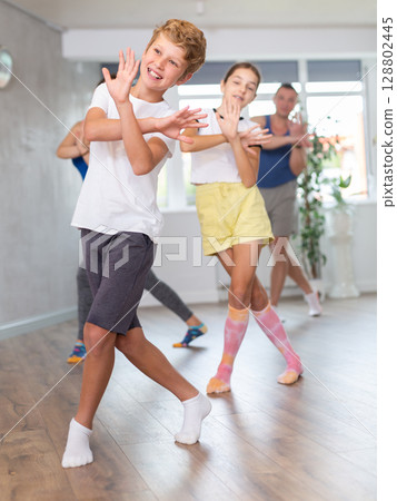 Excited preteen boy and girl exercising dance moves with their parents during dance class, family practicing dance with crossed hands in studio Excited preteen boy and girl exercising dance moves with their parents during dance class, family practicing dance with crossed hands in studio 128802445