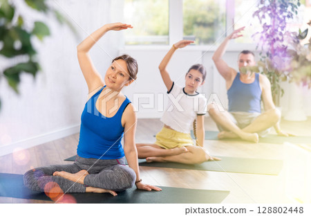 Happy middle-aged woman practicing half lotus pose of yoga with her family 128802448