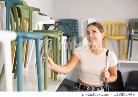 Woman in furniture center chooses plastic chairs for her apartment Woman in furniture center chooses plastic chairs for her apartment 128802449