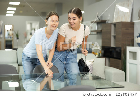 Female friends buyer choose dining table desk in furniture store showroom Female friends buyer choose dining table desk in furniture store showroom 128802457