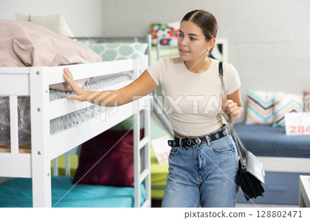 Young girl choosing new comfortable bunk bed in furniture store Young girl choosing new comfortable bunk bed in furniture store 128802471