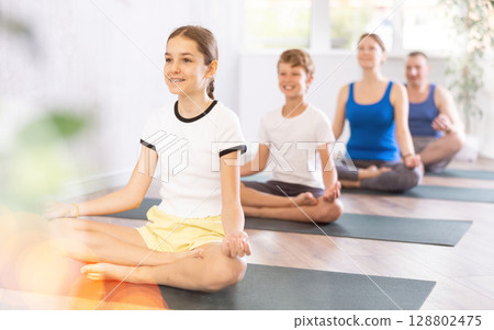 Pleasant preteen girl practicing lotus pose of yoga with her family Pleasant preteen girl practicing lotus pose of yoga with her family 128802475