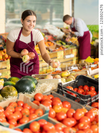 Friendly salesgirl offering ripe apples in fruit and vegetable store 128802476