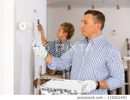 Father and son paint the walls of the room with paint roller 128802491