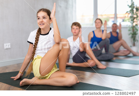 Friendly sporty parents with tween daughter and son performing Marichi position or Marichyasana on gymnastic mats barefoot in yoga studio. Family health concept 128802497