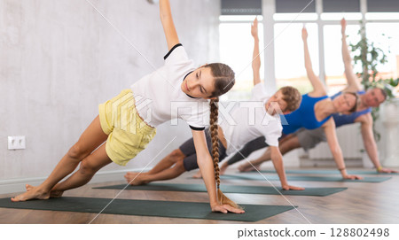 Kids and parents practicing Side Plank Pose or Vasisthasana on mats during family Hatha yoga class in studio Kids and parents practicing Side Plank Pose or Vasisthasana on mats during family Hatha yoga class in studio 128802498