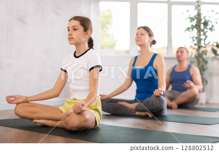 Pleasant preteen girl practicing lotus pose of yoga with her family 128802512