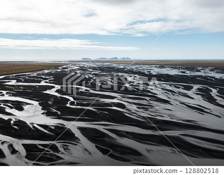 Aerial view of glacial river delta in Iceland Vestmannaeyjar with black sand patterns flowing into the ocean. Concept of raw earth, climate forces, water systems, natural design and Arctic minimalism. 128802518