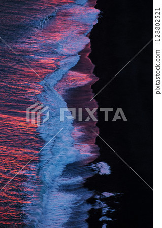 Waves reflecting pink sunset light crash onto black sand beach in Iceland. Concept of natural contrast, visual balance, energy, minimalism, and emotional stillness. Waves reflecting pink sunset light crash onto black sand beach in Iceland. Concept of natural contrast, visual balance, energy, minimalism, and emotional stillness. 128802521