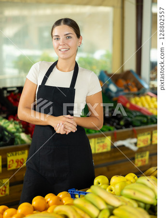 Positive and friendly store girl employee stands with arms crossed on chest and waits for customers Positive and friendly store girl employee stands with arms crossed on chest and waits for customers 128802557