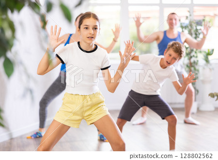 Happy preteen boy and girl practicing dance movements with their parents 128802562