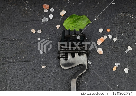 black pasta with cuttlefish ink and green basil leaves on a black fork. Pasta of durum wheat semolina with squid ink. 128802784