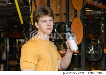 Portrait of bodybuilder or sporty young caucasian man with protein shake in hand. Athlete and professional trainer with sports nutrition beverage while working out. Portrait of bodybuilder or sporty young caucasian man with protein shake in hand. Athlete and professional trainer with sports nutrition beverage while working out. 128802985