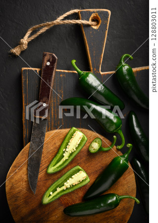 Black jalapeno hot peppers on wooden cutting board 128803011