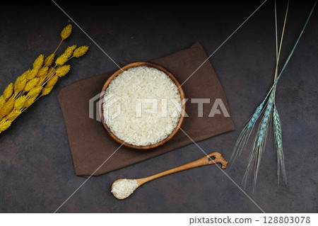 Raw white rice on black background. Long uncooked rice in wooden plate. Natural organic food. Traditional Asian cereal culture. 128803078