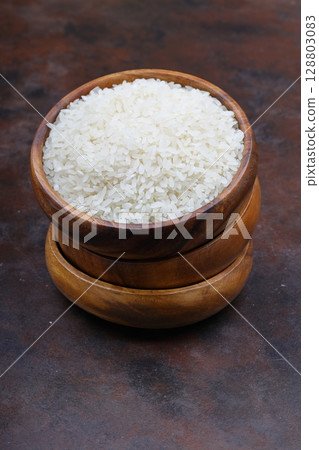 Raw white rice on black background. Long uncooked rice in wooden plate. Natural organic food. Traditional Asian cereal culture. 128803083