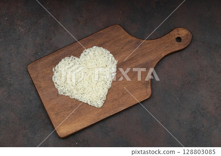 Heart-shaped rice on dark background. Love and valentines day concept. Raw long white rice in shape of heart. Traditional Asian food. Heart-shaped rice on dark background. Love and valentines day concept. Raw long white rice in shape of heart. Traditional Asian food. 128803085
