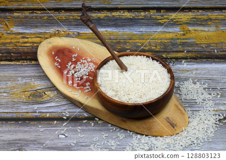 Raw white rice on black background. Long uncooked rice in wooden plate. Natural organic food. Traditional Asian cereal culture. Raw white rice on black background. Long uncooked rice in wooden plate. Natural organic food. Traditional Asian cereal culture. 128803123