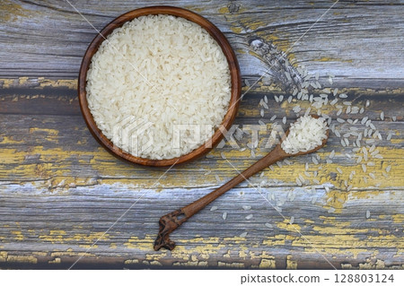 Raw white rice on black background. Long uncooked rice in wooden plate. Natural organic food. Traditional Asian cereal culture. 128803124