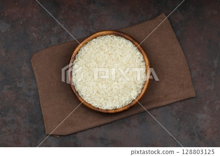 Raw white rice on black background. Long uncooked rice in wooden plate. Natural organic food. Traditional Asian cereal culture. Raw white rice on black background. Long uncooked rice in wooden plate. Natural organic food. Traditional Asian cereal culture. 128803125
