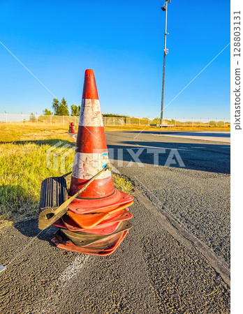Worn airport traffic cone with wheel chocks and blue sky on asphalt road. High quality photo 128803131