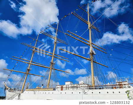 Sailing ship with tall masts and flags under bright blue sky with clouds. High quality photo 128803132