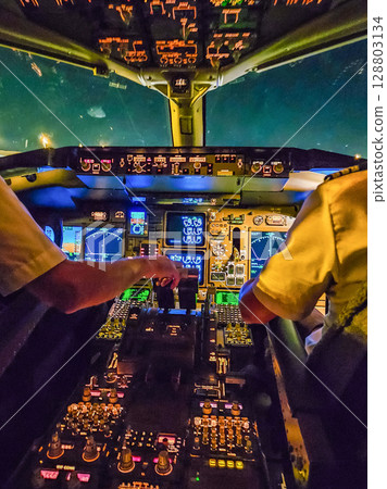 Pilots operating aircraft cockpit illuminated by control panel lights at night. High quality photo 128803134