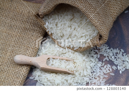 Raw white rice on black background. Long uncooked rice in wooden plate. Natural organic food. Traditional Asian cereal culture. 128803140
