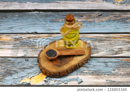 Black cumin seeds and essential oil with bowl and wooden shovel or spoon. Nigella Sativa in glass bottle. Organic herbal medicine for many diseases 128803160