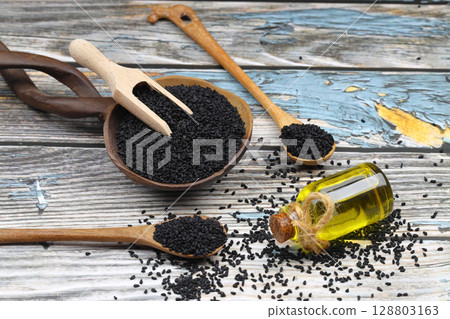 Black cumin seeds and essential oil with bowl and wooden shovel or spoon. Nigella Sativa in glass bottle. Organic herbal medicine for many diseases 128803163