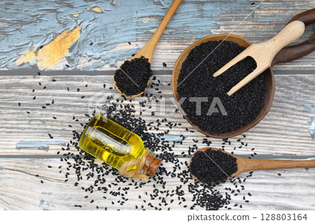 Black cumin seeds and essential oil with bowl and wooden shovel or spoon. Nigella Sativa in glass bottle. Organic herbal medicine for many diseases 128803164