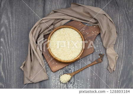 Top view closeup of freshly harvested white sesame in wooden bowl isolated on wooden background with clipping path. 128803184