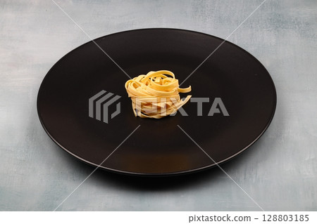 Uncooked tagliatelle in a black plate Uncooked tagliatelle in a black plate 128803185