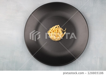 Uncooked tagliatelle in a black plate Uncooked tagliatelle in a black plate 128803186