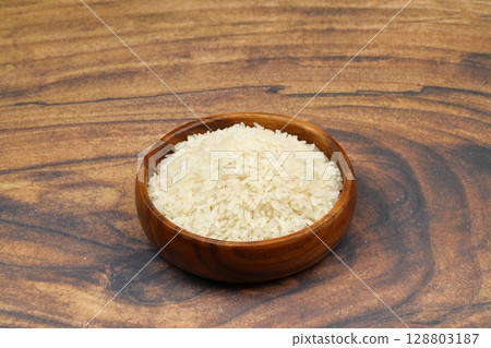 Raw white rice on black background. Long uncooked rice in wooden plate. Natural organic food. Traditional Asian cereal culture. Raw white rice on black background. Long uncooked rice in wooden plate. Natural organic food. Traditional Asian cereal culture. 128803187