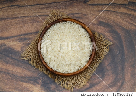 Raw white rice on black background. Long uncooked rice in wooden plate. Natural organic food. Traditional Asian cereal culture. Raw white rice on black background. Long uncooked rice in wooden plate. Natural organic food. Traditional Asian cereal culture. 128803188